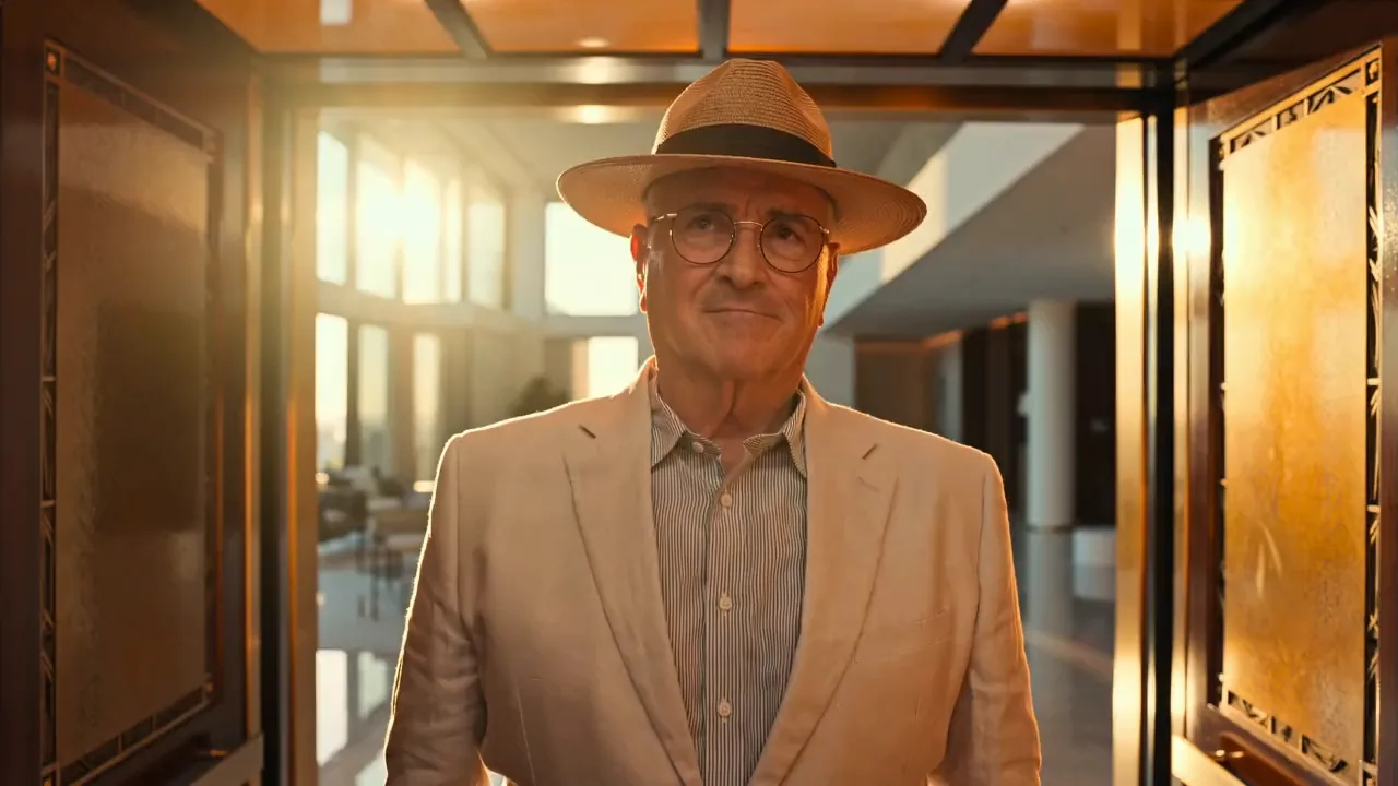 Joe Goodman in a linen suit and straw hat in an elevator as the doors open onto a bright lobby, from his film